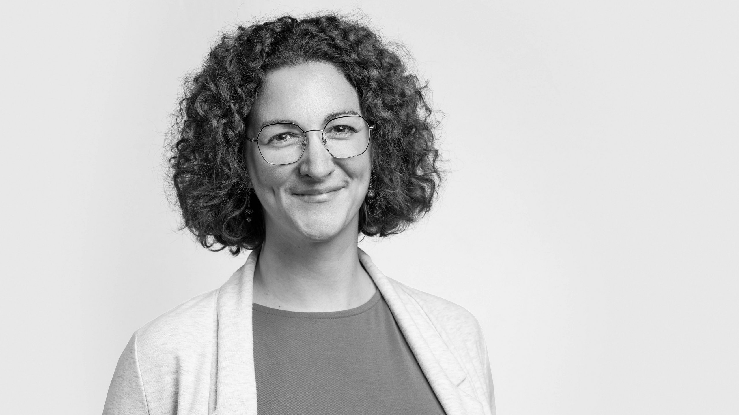 [Translate to Englisch:] Schwarz-weißes Portrait von Sara Leicht vor grauem Hintergrund